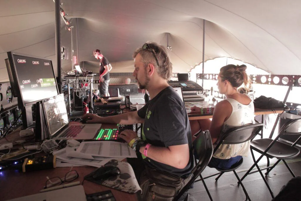 Production team operating laptops and audiovisual equipment inside an event tent.