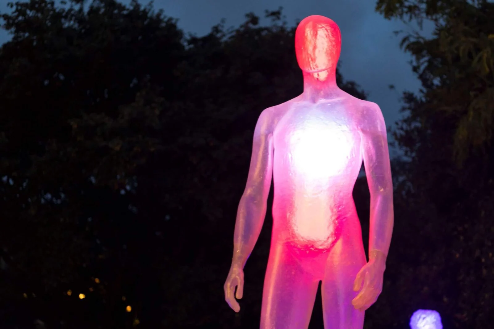 Translucent human figure glowing pink and white against the dark outdoor setting.