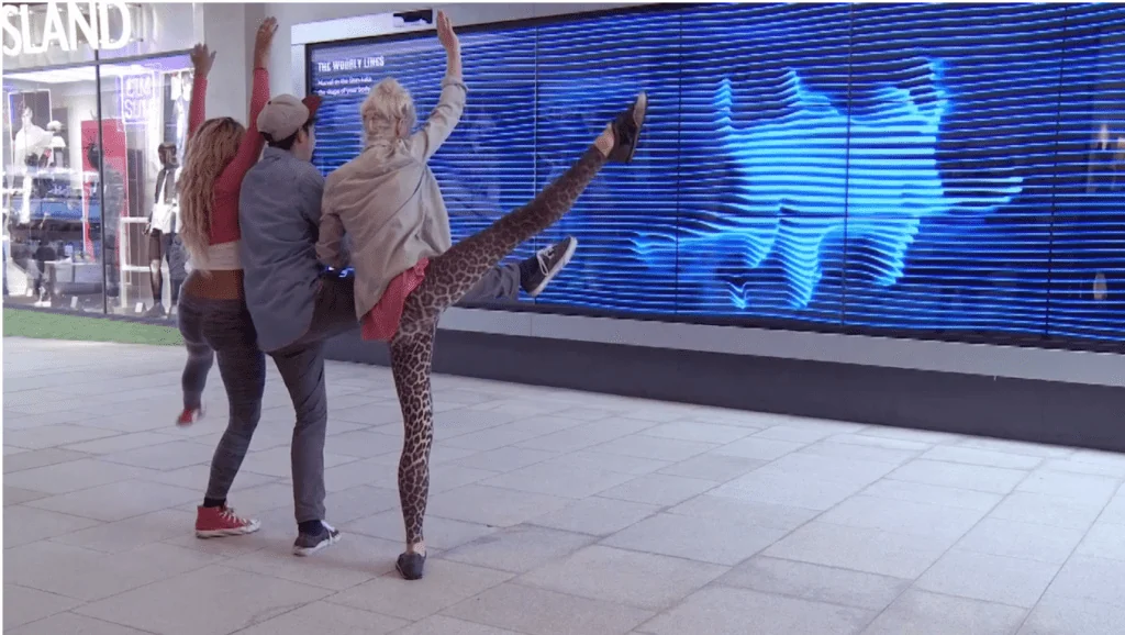 Visitors posing in front of a blue video wall that echoes their silhouettes.