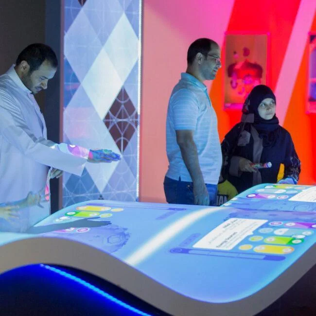 Visitors playing Energy Manager on a curved table covered with projected game graphics.