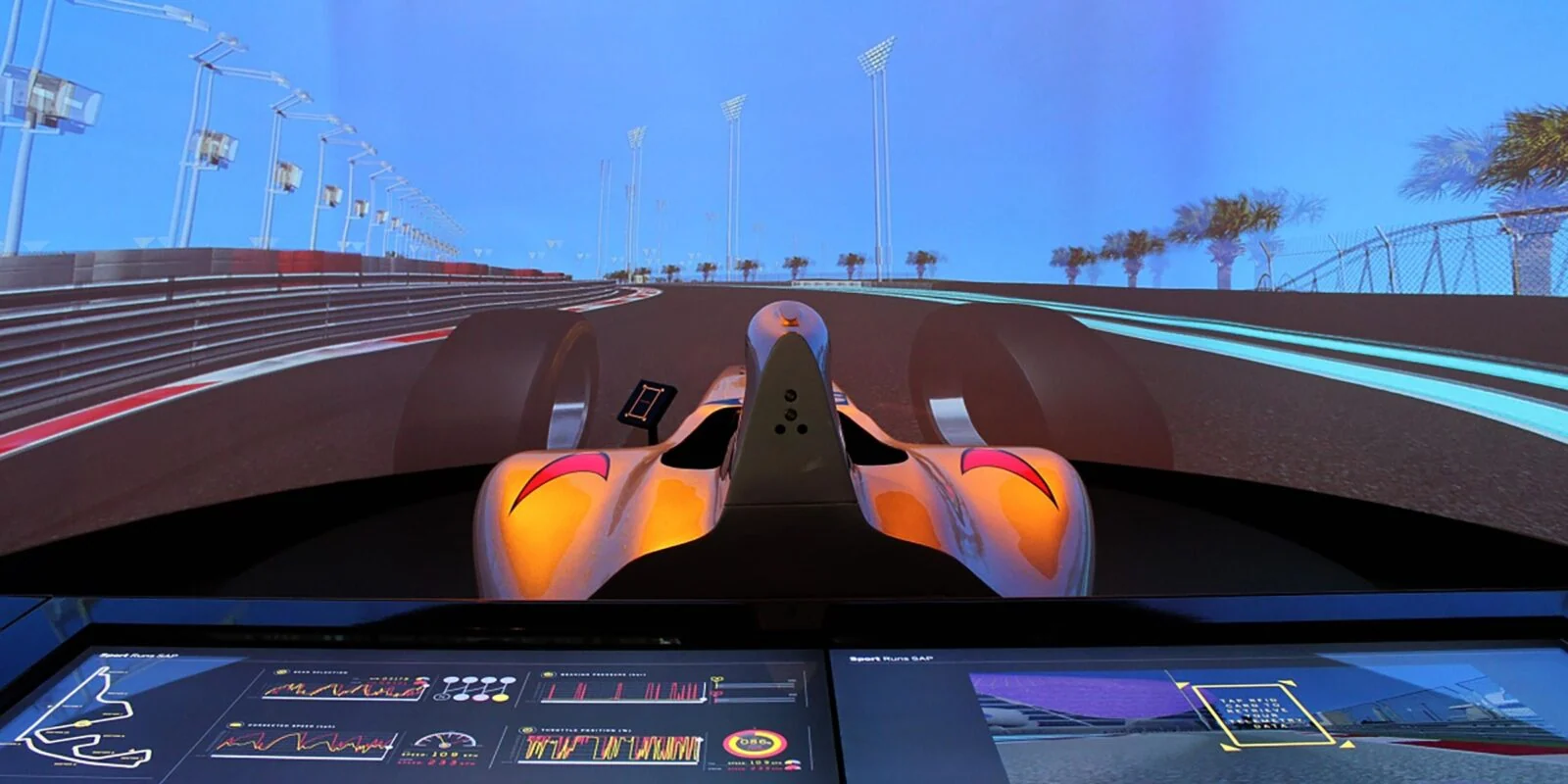 Panoramic racing display with an orange car and a touchscreen dashboard below.