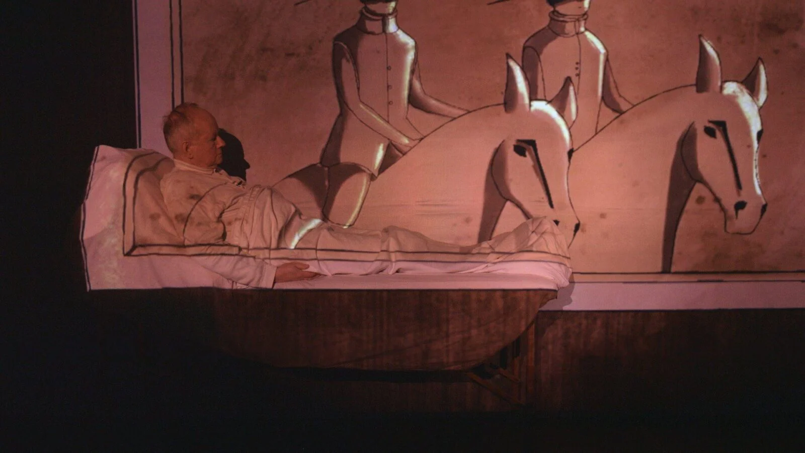 Performer on a bed with a projected hand-drawn horse and carriage scene.